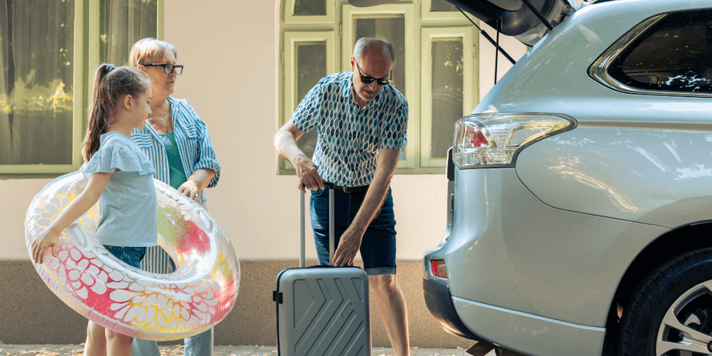 A man arranging his suitcase next to a car while his family stands nearby, ready for their journey.